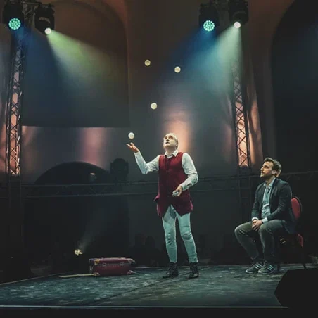 Stephan Masur interaktiber barocker Jongleur & Zeremonienmeister Zwei Männer auf einer Bühne; einer jongliert mit Bällen, der andere sitzt daneben.