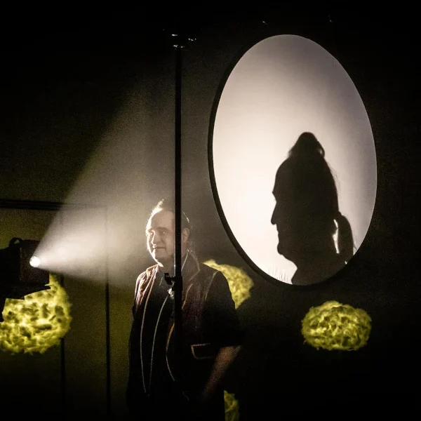 Stephan Masur Schattenshow Barockkünstler Mann steht im Licht mit Schatten auf der Wand, hinter einer großen, runden Leinwand.